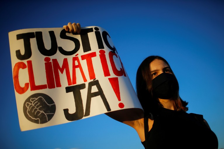 A demonstrator wearing a black face mask holds a sign reading "Climatic justice now" in Portuguese