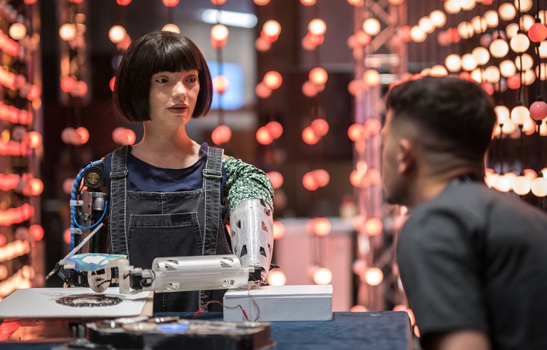 Man sitting at a table faces the female robot Ai-Da during an international summit in Geneva.