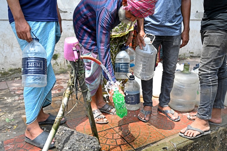 Low-angle view of people gathered around a roadside water pipeline collecting drinking water