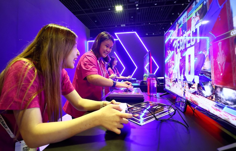 Two women laugh while playing a Street Fighter game at a convention centre in Singapore.