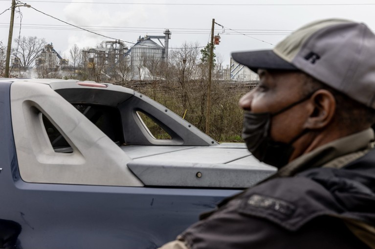 A resident of Gloster, Mississippi, wearing a face maskstandins next to a vehicle with a biomass production plant in the background