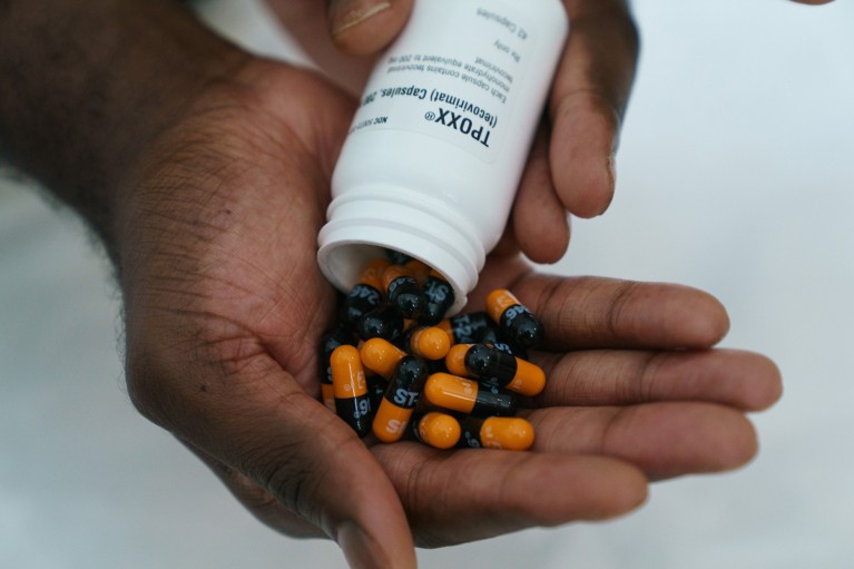 Closeup of someone emptying a bottle of orange and black tecovirimat pills into their open palm