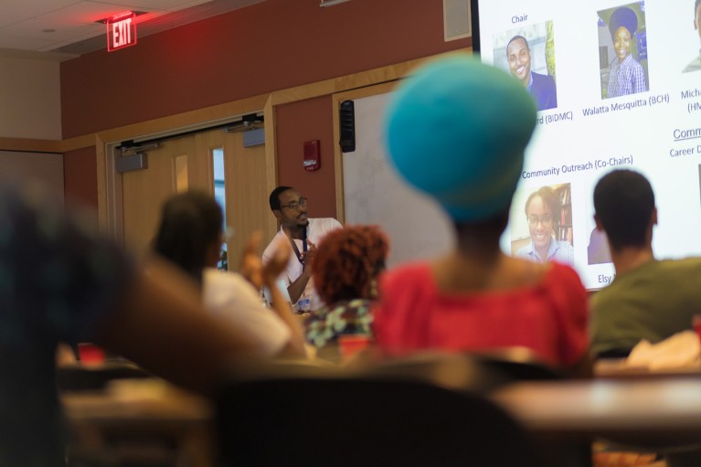 Frankie Heyward gives a speech to an audience while looking at a projector screen