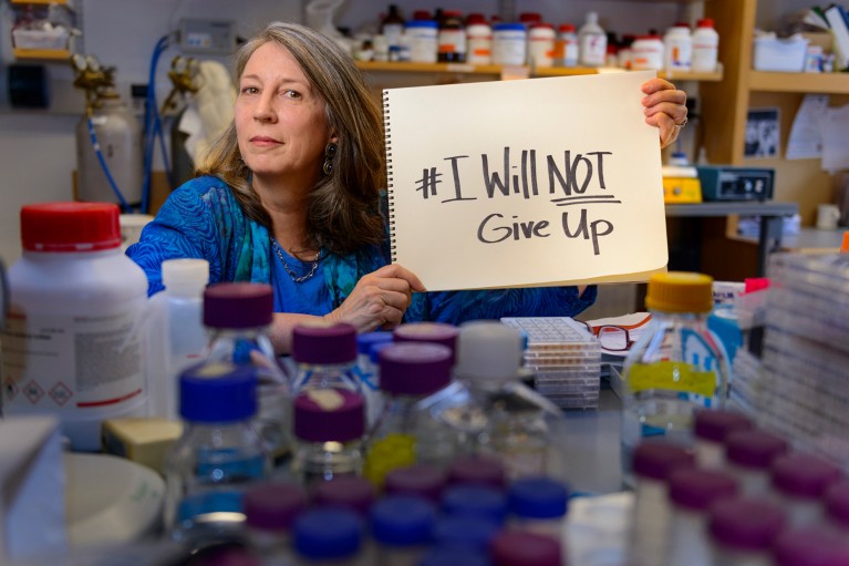 Terry Jo Bichell in a lab surrounded by many bottles holding a notepad with "I will not give up" handwritten on it