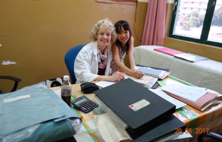 Woman in a white coat sitting near a little girl sitting in an office in a Sri Lanka clinic.