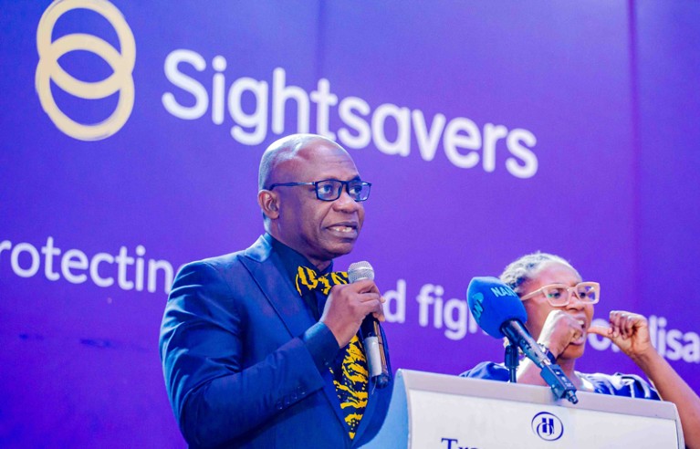 Sunday Isiyaku speaks at a Sightsavers event with sign language interpreter in background"