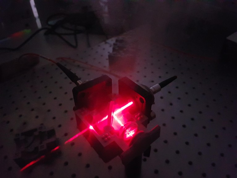 A pink laser is shown through lenses in a laboratory