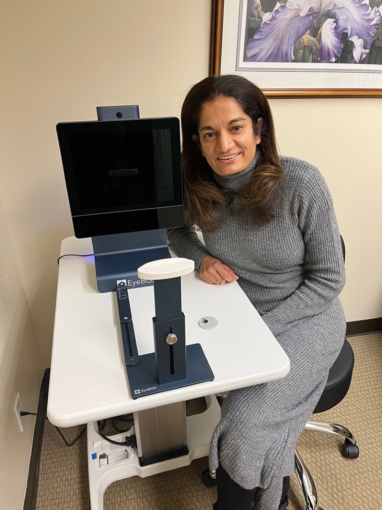 Uzma Samandi seated next to the Oculogica device; a large screen with chin rest.