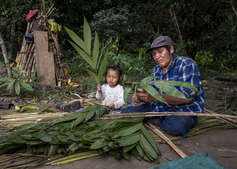 A man and small child sit together weaving palms in the Bolivian Amazon