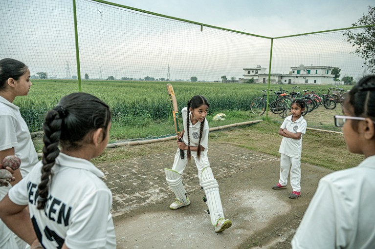 Members of a girls cricket team in India watch their team mate in shin pads practicing her batting technique