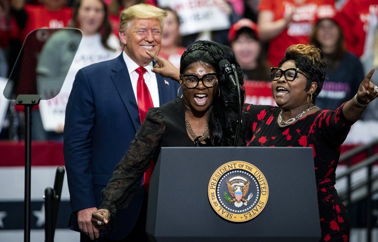 Two Black women, social media influencers and video bloggers speak as U.S. President Donald Trump smiles during a rally.