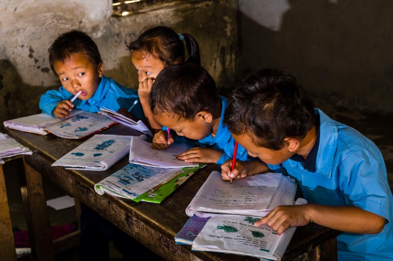 Young pupils in a school in Nepal sitting at a desk working in exercise books