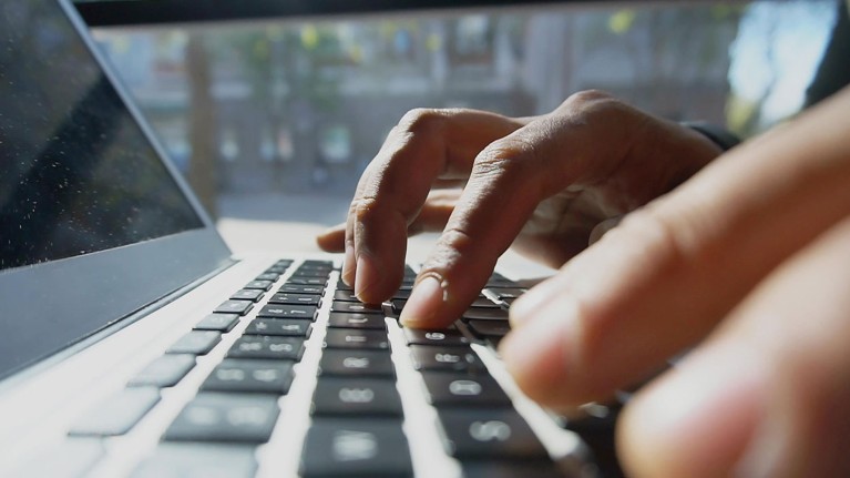 Vista cercana de las manos de un hombre escribiendo palabras en el teclado de una computadora portátil.