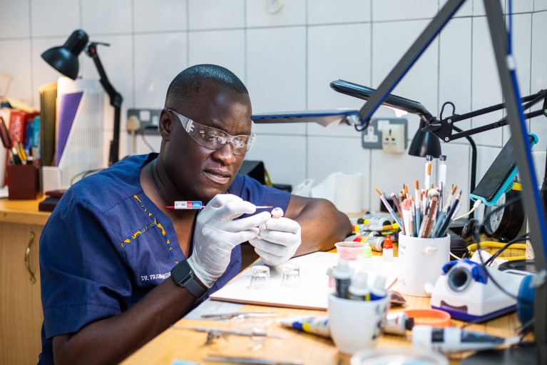 Franklin Wasswa wears protective glasses and gloves while hand painting a custom ocular prosthetic in his workshop