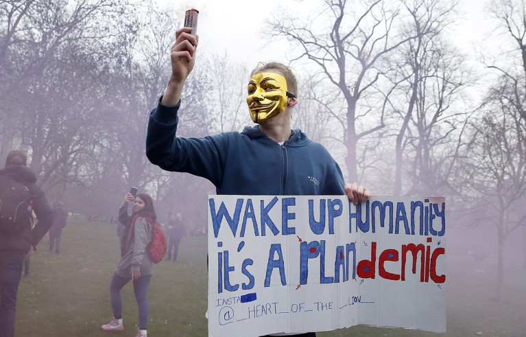 A protester with a flare poses holding a sign calling for people to "wake up" during a "World Wide Rally For Freedom" protest in London, England.