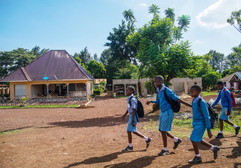 Children in blue school uniforms walk along an unpaved road In Tanzania