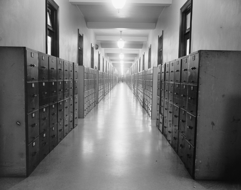 A black and white photograph of a hallway lined with old filing cabinets