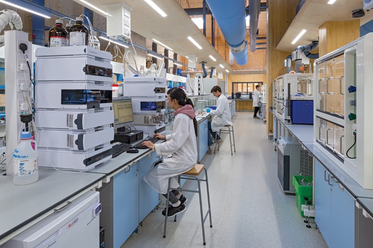 Science lab with wooden walls. White-coated researchers are working at benches.