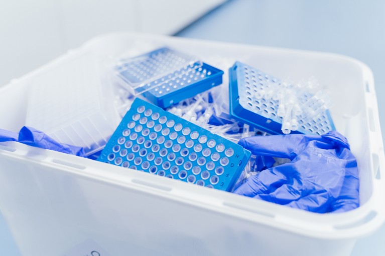 Close-up of blue plastic micro plates and white plastic tubes, along with blue surgical gloves in a bin.