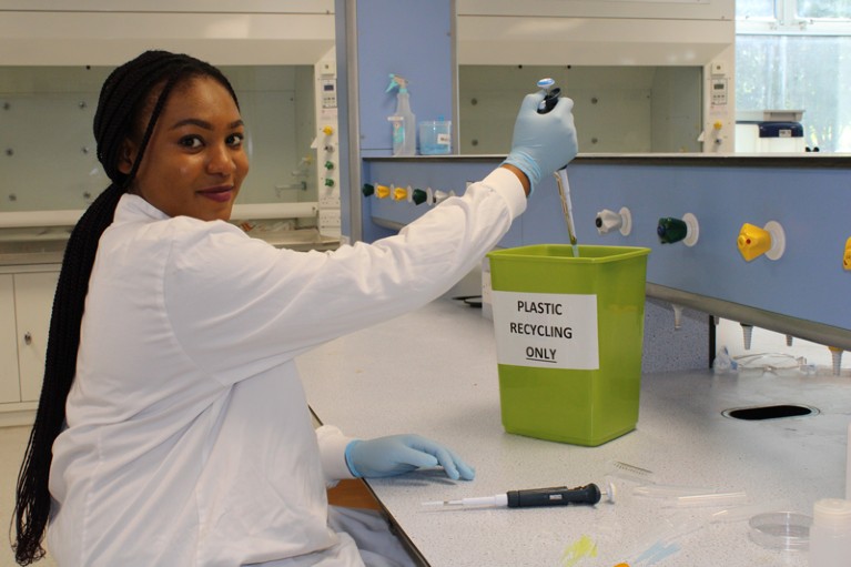 A student is depositing a pipette into a green recycle bin.