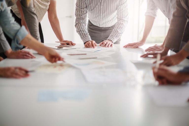 Low angle view of hands of a group of people working together around a table of paper documents.