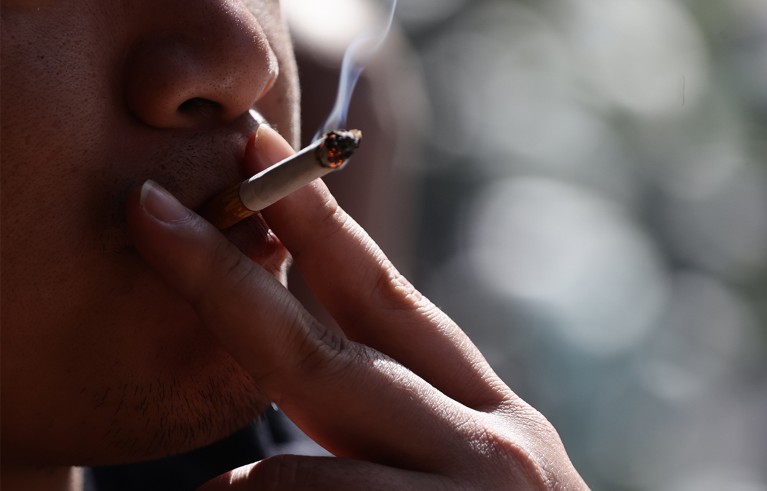 Close-up of someone holding a cigarette closer to the mouth in a cloud of smoke.