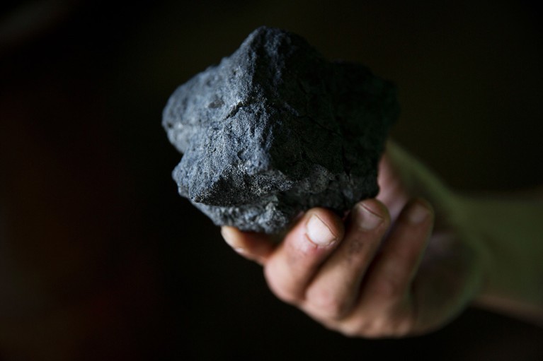 Close up view of a hand holding a lump of coal.