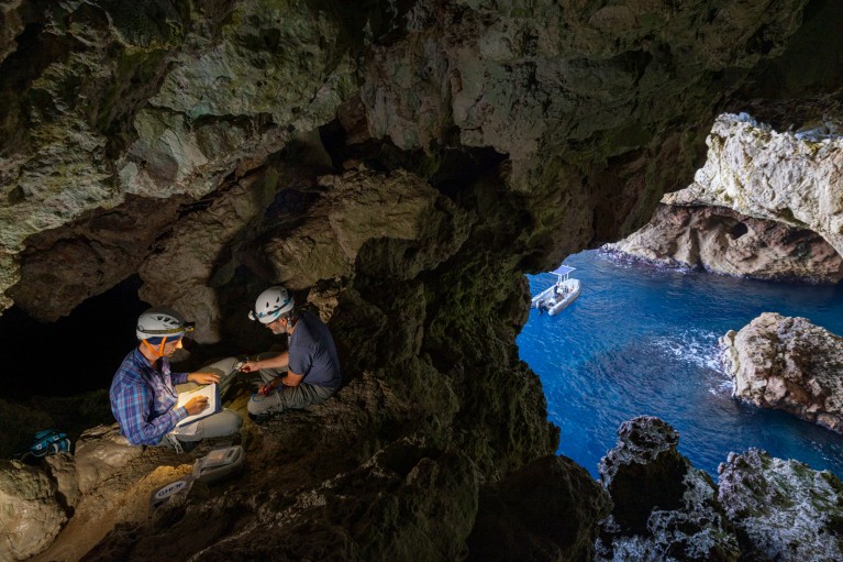 Federico De Pascalis and a colleague, wearing hard hats with head torches, sit on a ledge in a sea cave documenting storm petrol birds