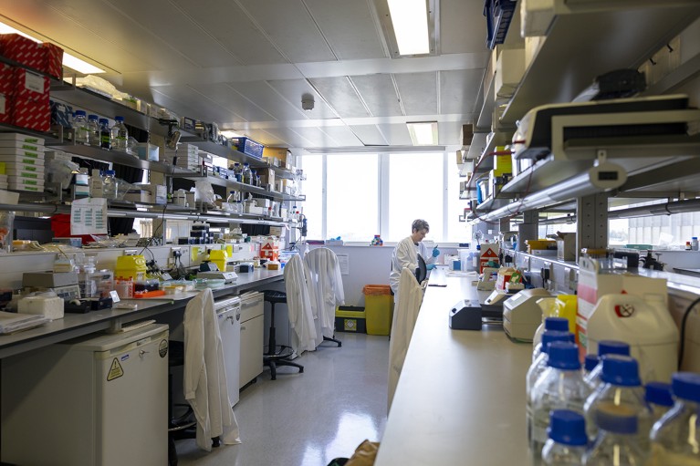 A researcher wearing a lab coat and holding science equipment in a lab.