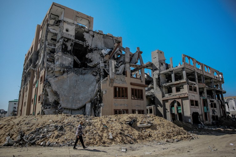 A man walks past a pile of rubble and a heavily damaged multi storey building which is part of the Islamic University in Gaza City