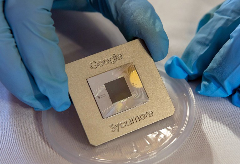 A Google quantum processor "Sycamore" is held by a pair of hands in protective gloves.