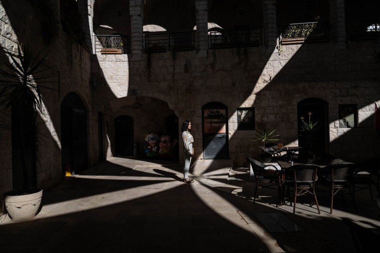 Mona Demaidi standing in the middle of a dark courtyard surrounded by areas of shadow and light