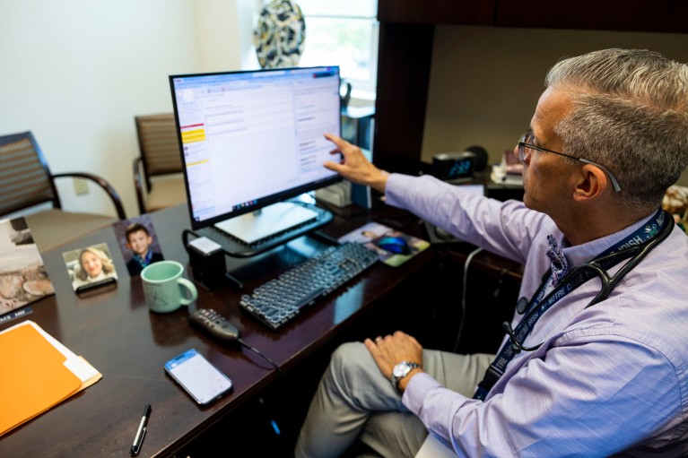 A doctor points to a transcription on his computer screen at his desk