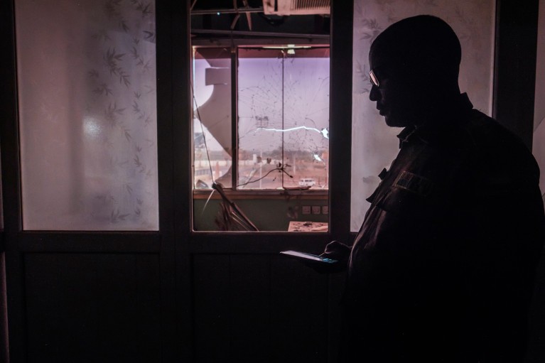 A man looks at his mobile phone while standing in a dark office in hospital building with broken windows in Sudan