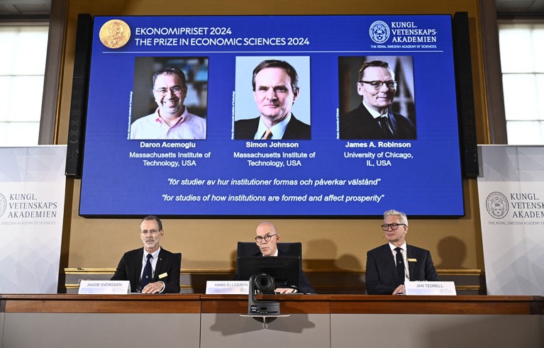 Academy of Sciences permanent secretary Hans Ellegren (C), Jakob Svensson (L) and Jan Teorell of the Nobel Assembly sit in front of a screen displaying the laureates (L-R) Turkish-American Daron Acemoglu and British-Americans Simon Johnson and James Robinson of the 2024 Sveriges Riksbank Prize in Economic Sciences.