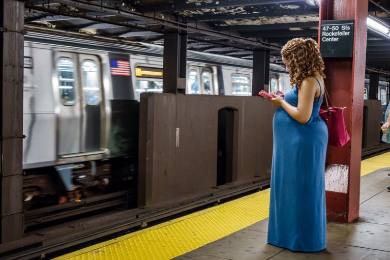 A pregnant woman looking at her phone while waiting for a New York subway train