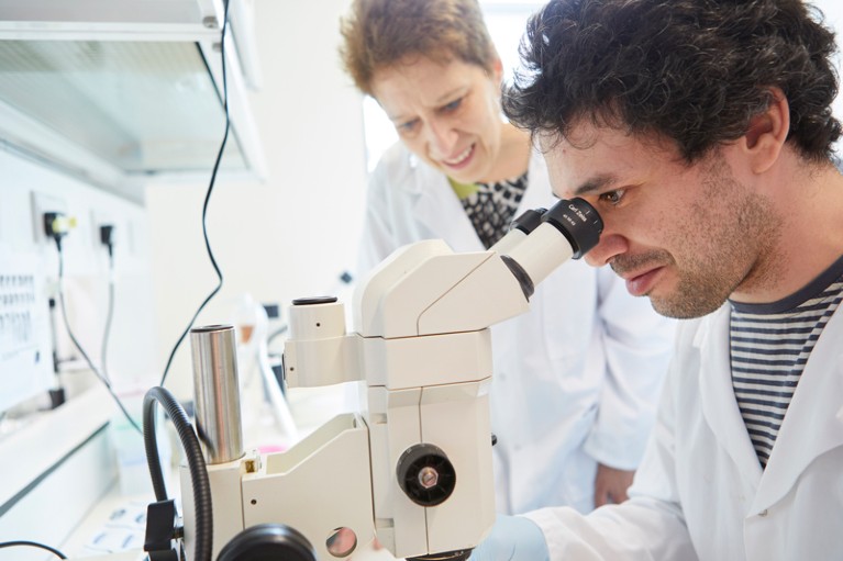 Caroline Hill and postdoc Andrew Economou looking down a microscope in the la