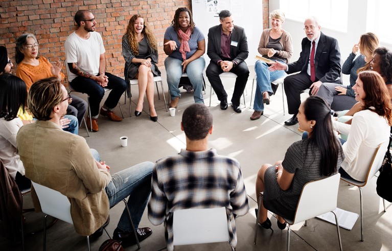 A large group of work colleagues sat in a circle hold a strategy discussion.