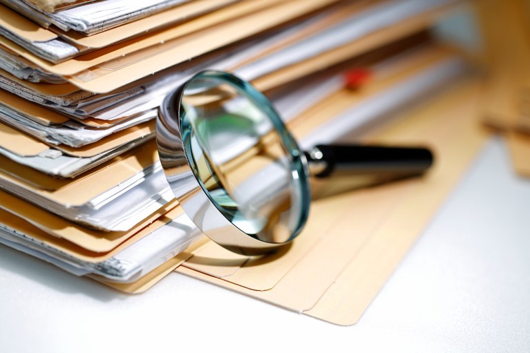 Close up view of a magnifying glass resting on a stack of paper documents in folders.