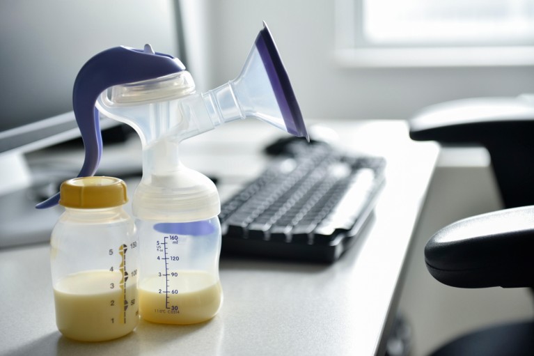 A breast pump and bottle of breast milk on a desk with a computer monitor and keyboard