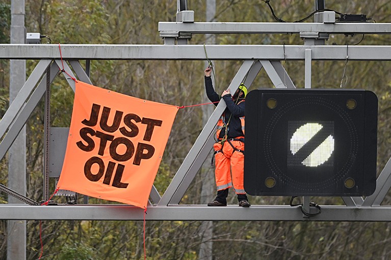 n activist puts up a banner reading "Just Stop Oil" atop an electronic traffic sign along M25