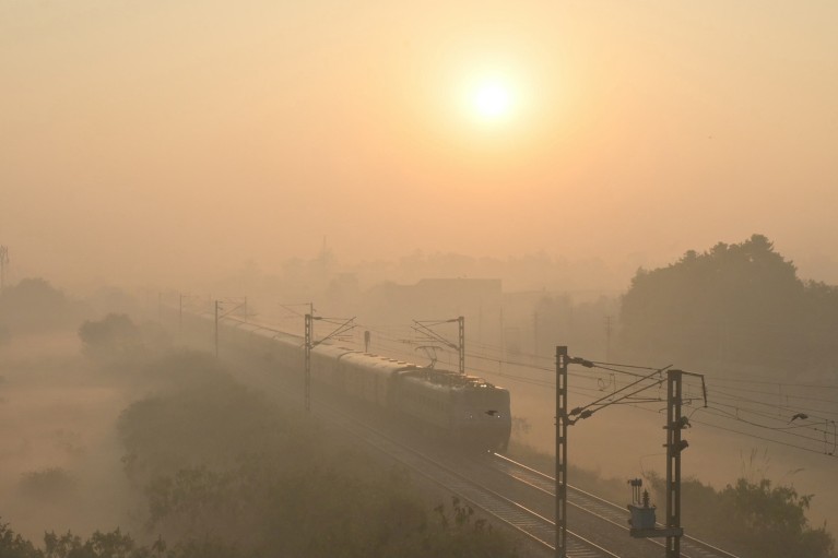 A train passes through heavy smog on the outskirts of Amritsar, with the sun creating an ethereal glow