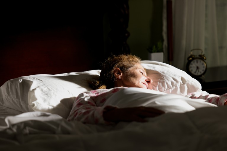 A woman lies in bed asleep with sunlight shining on her face