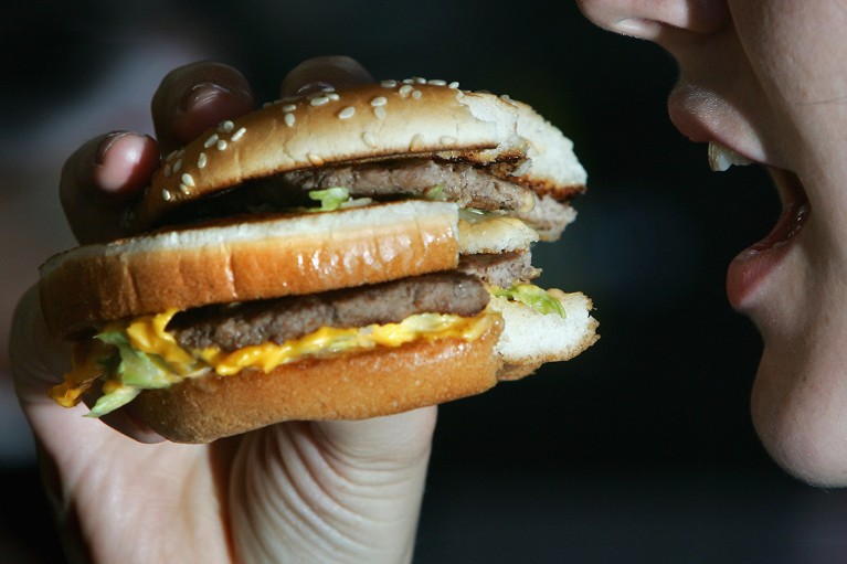 Vista cercana de una mujer a punto de morder una hamburguesa a medio comer.