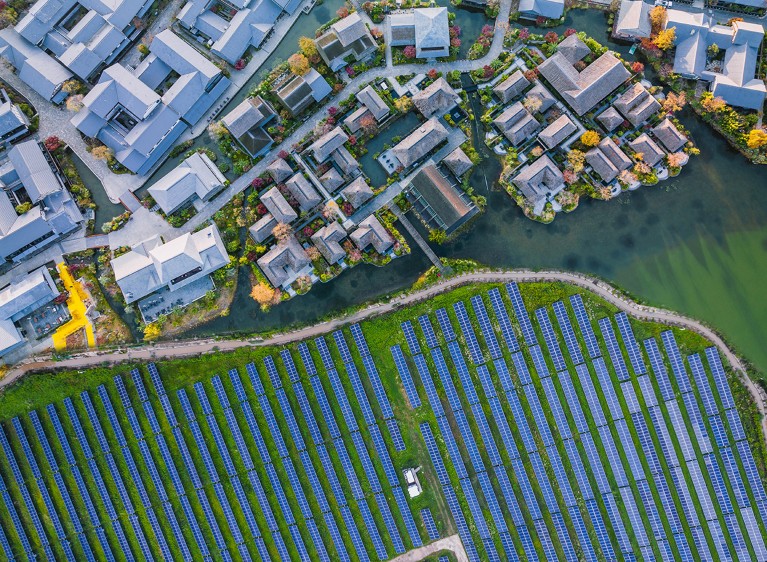 Aerial view of buildings in the top half of the image, and solar panels in the bottom half.