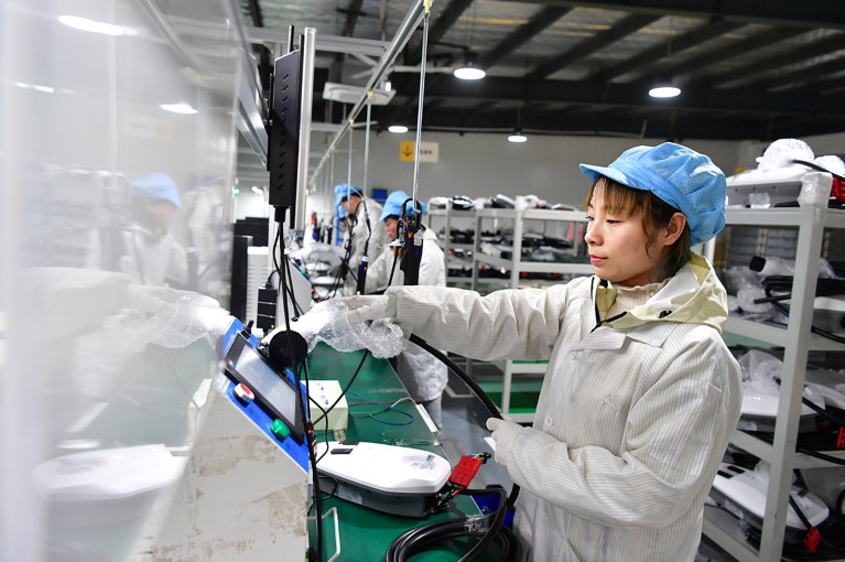 Una donna cinese che indossa un cappello blu e un camice bianco sta lavorando su una linea di produzione in fabbrica.