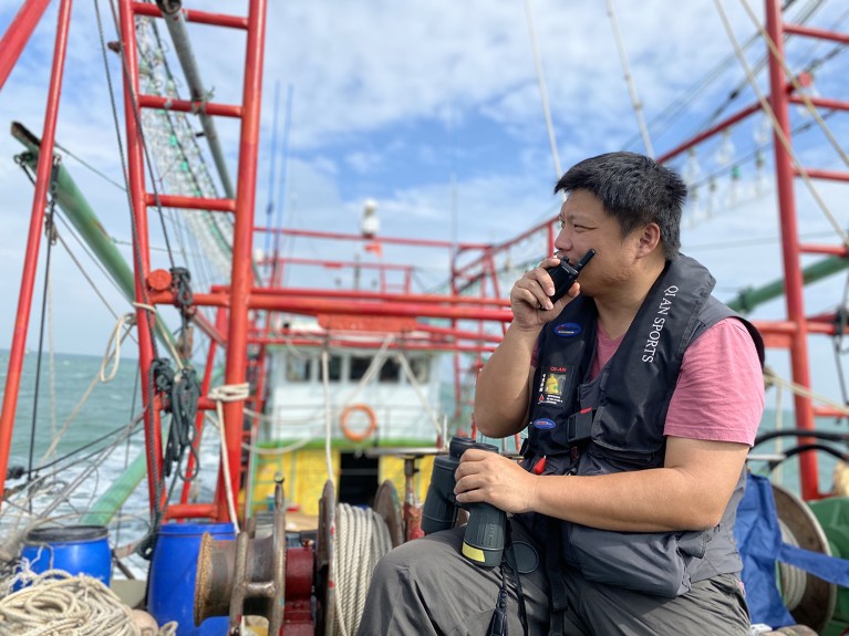 Chen Mo on a ship using a handheld radio to communicate while searching for whales.