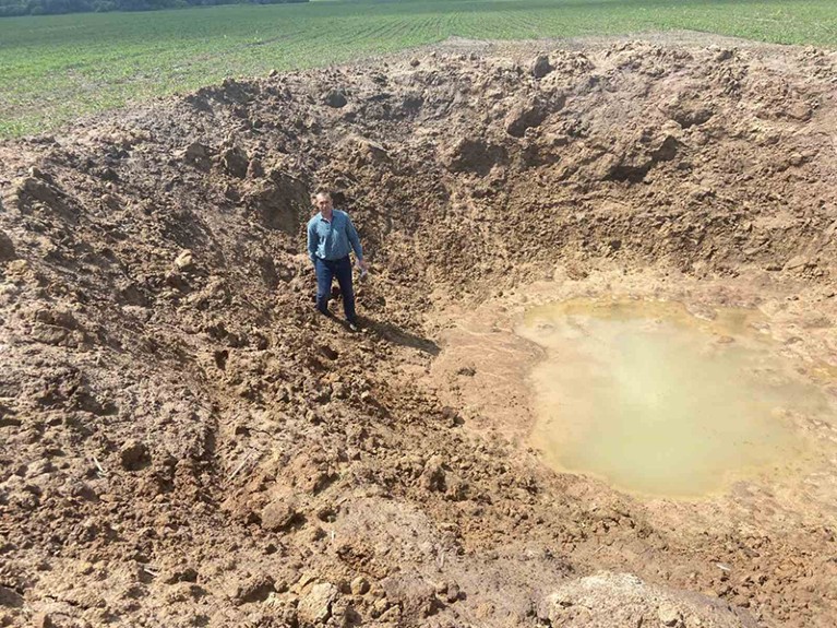 Una foto di Igor Kovalenko in piedi nel cratere di una bomba