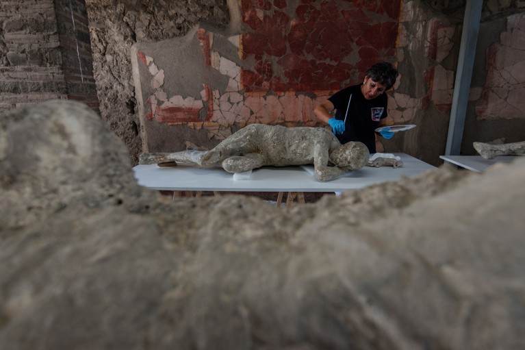 A restorer wearing blue gloves works on a petrified victim laying on a table