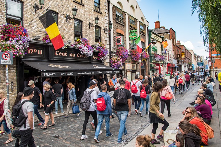 Crowds of people walking past a pub on a busy side street.